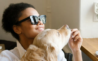 Woman wearing sunglasses smiling while giving a golden retriever scratches on the muzzle